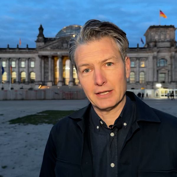 Person står framför riksdagshuset i Berlin under kvällstid.