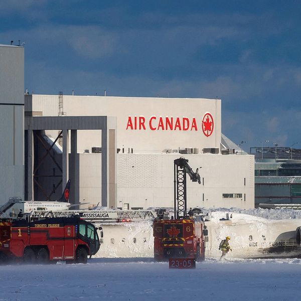 Räddningsfordon vid ett flygplansvrak framför Air Canadas hangar i vintrigt landskap.