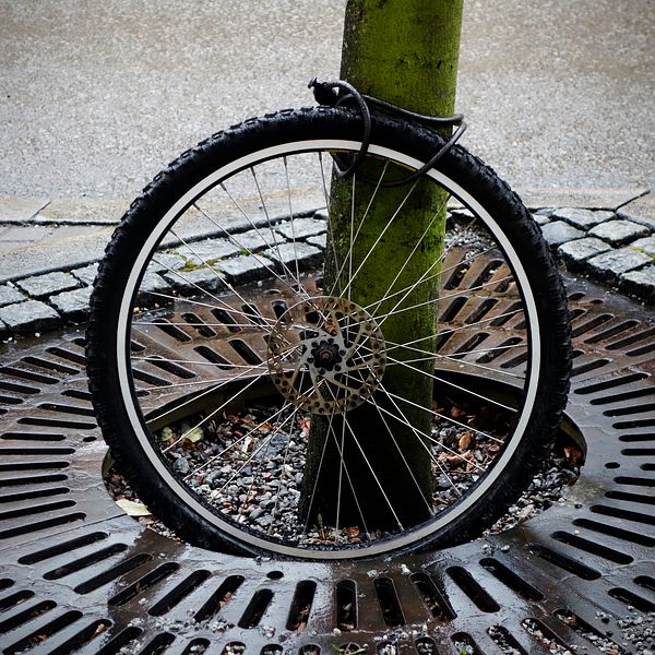 Ensamt cykelhjul fastlåst vid en stolpe på trottoaren.