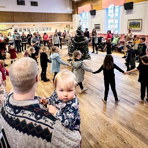 En massa folk dansar runt en julgran i Tandsbyn