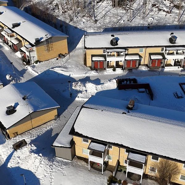 Flygbild över snötäckt bostadsområde med radhus och snöiga gångvägar.