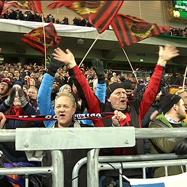 Fotbollsfans hejar och viftar med flaggor på en läktare.