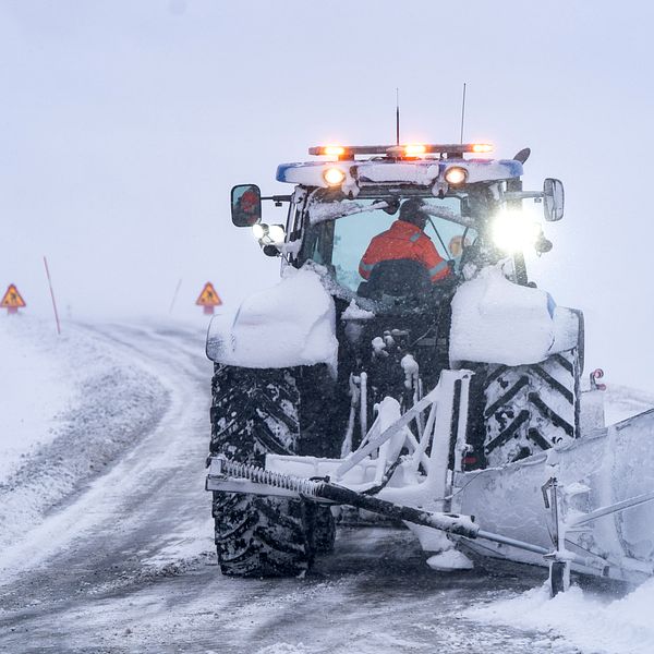 Traktor plogar en snöig landsväg under dimmiga förhållanden.