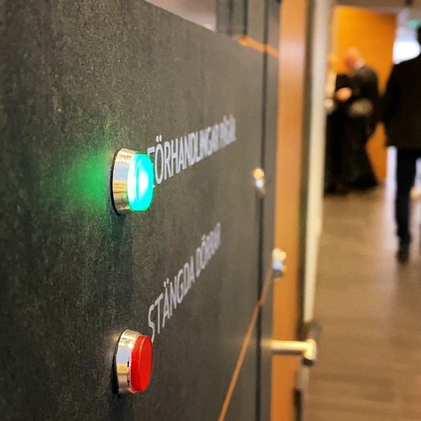 Personer går in i en sal i Växjö tingsrätt. En lampa med texten förhandlingar pågår lyser grönt.