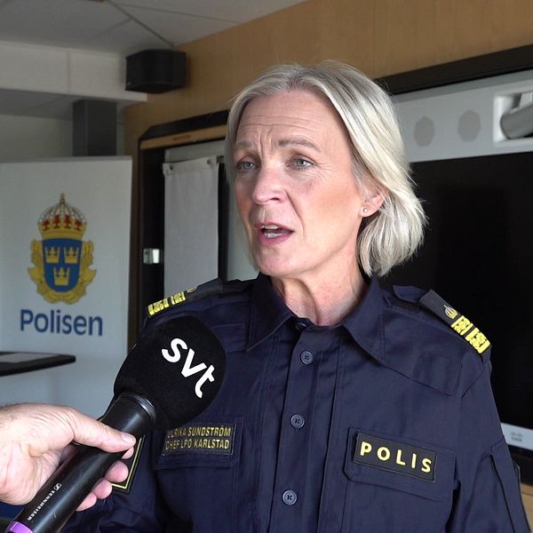 En polis med en svensk polisuniform blir intervjuad av en journalist som håller en mikrofon märkt med ”SVT”. I bakgrunden syns en växt, en TV-skärm och en skylt med Polisens logotyp.