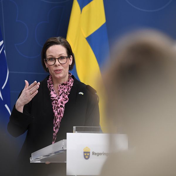 En person talar vid podiet med NATO och svenska flaggan i bakgrunden.