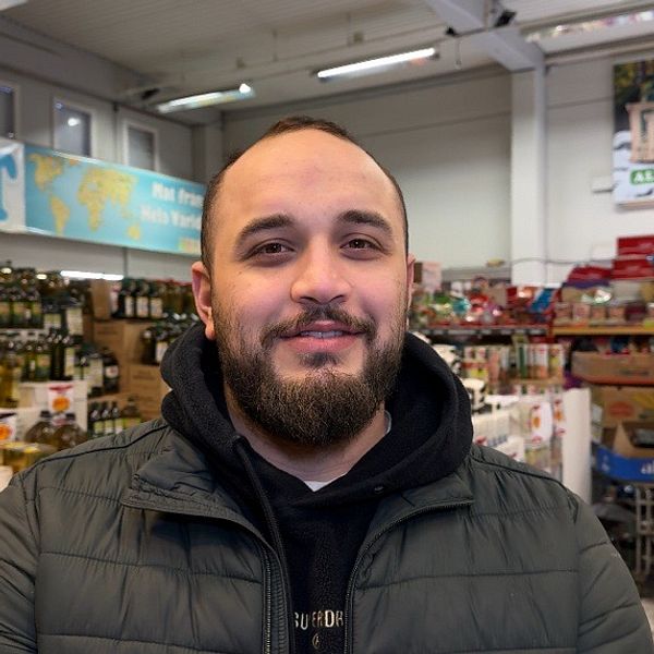 Man i grön jacka står framför hyllor i en matbutik.
