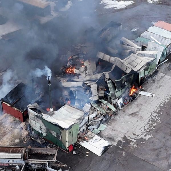 Brand vid en anläggning, stora mängder rök stiger från ett nedbrunnet garage.