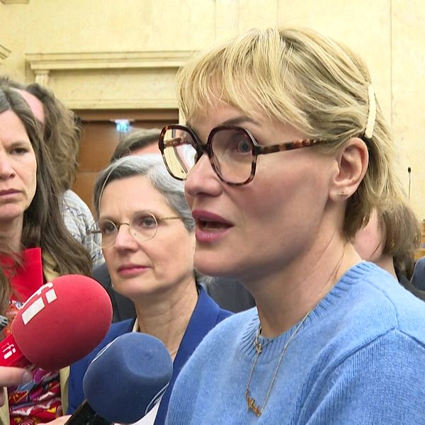 Journalister intervjuar en person inomhus, mikrofoner riktade mot den.
