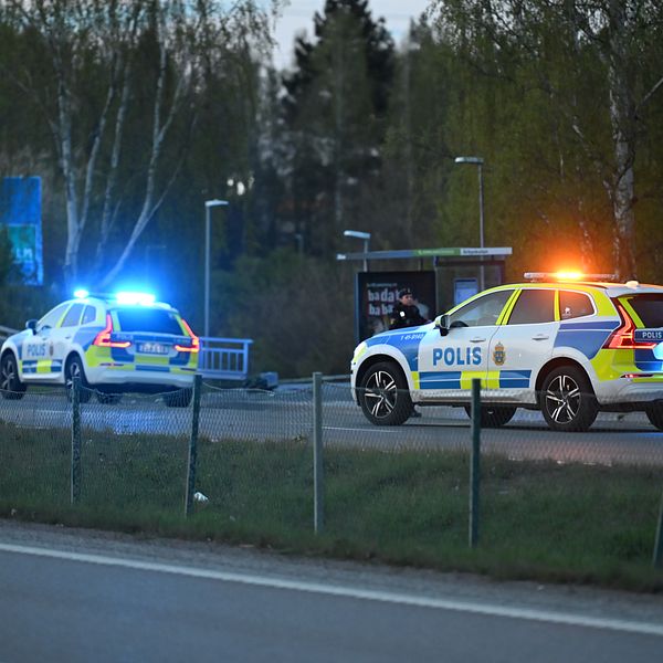 Två svenska polisfordon med blåljus står vid vägkant nära en rondell på kvällen.