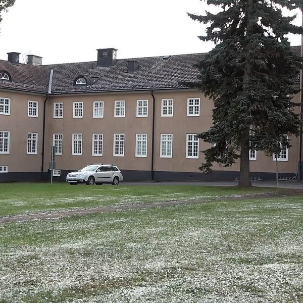 En byggnad av tegel med snö på marken framför, en vit bil står parkerad.