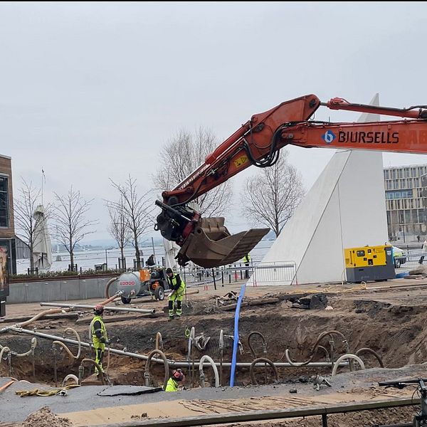 Grävmaskin arbetar på byggarbetsplats nära modern byggnad.