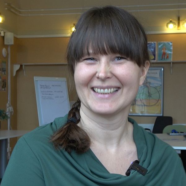 Maria Östlund i grön tröja sitter i ett klassrum. Whiteboard och affischer syns i bakgrunden.