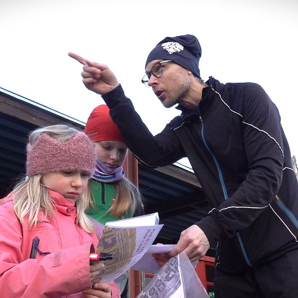 En pappa beskriver för sina döttrar hur man ska läsa kartorna inför starten på parkorienteringen.