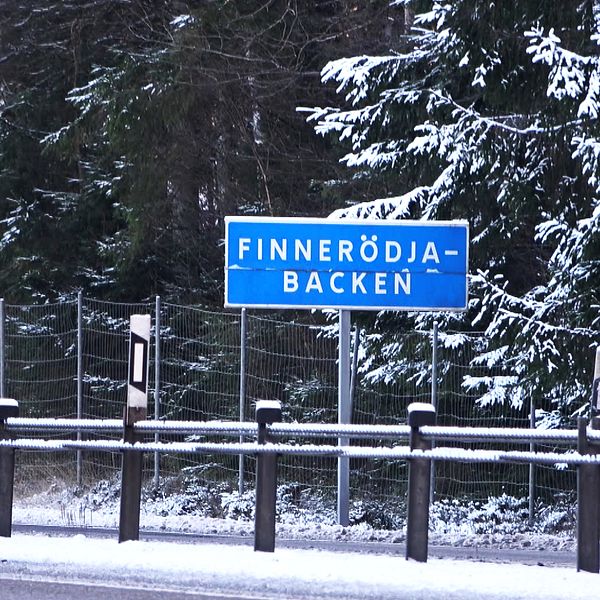 Skylt som visar namnet ”Finnerödja-Backen” vid en snöig väg nära en tät skog.