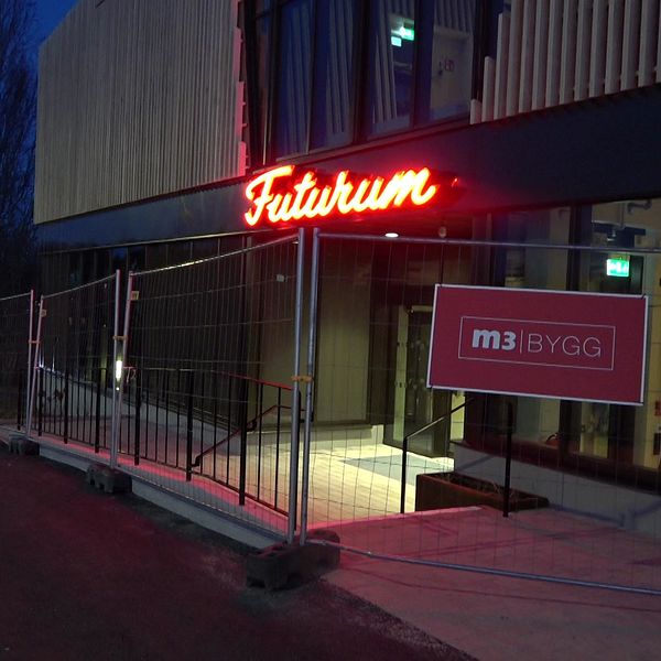 Det är kväll och den gamla neonskylten som lyser gult/orange Futurum i skrivstil. Byggnaden är omgiven av ett byggstaket