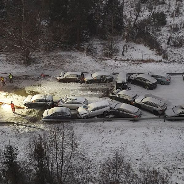 Flera bilar krockade på en snöbelagd väg, med en bogserbil synlig på platsen som arbetar för att rensa upp efter olyckan. Ledningar och skog kantar vägen.