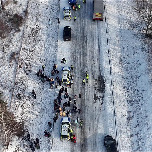 Vinterlandskap med bilkö och människor vid olycksplats på snötäckt väg.