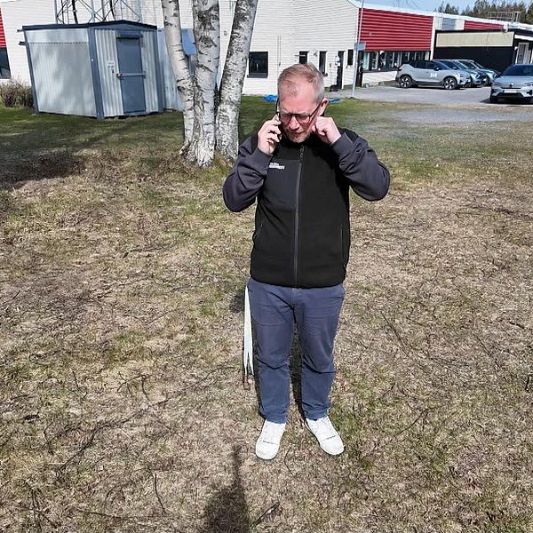 En man står utomhus på en gräsmatta och sätter på sig glasögon.