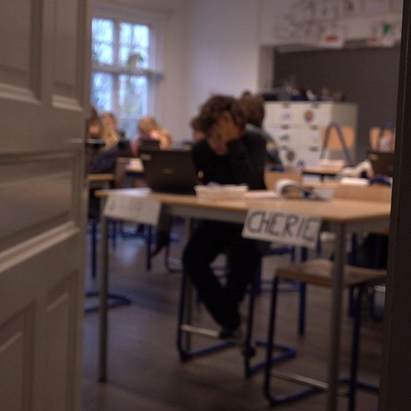 Ett klassrum där bilden är suddig, man ser elever och bänkar.