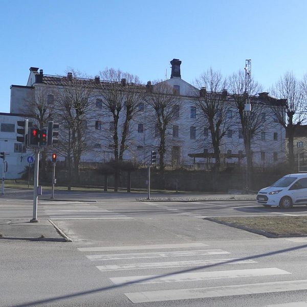 Gatukorsning med en vit skåpbil framför en stor byggnad och träd utan löv.