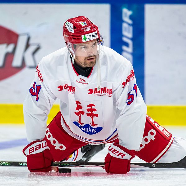 Hockeyspelare i vit och röd dräkt stretchar på isen.