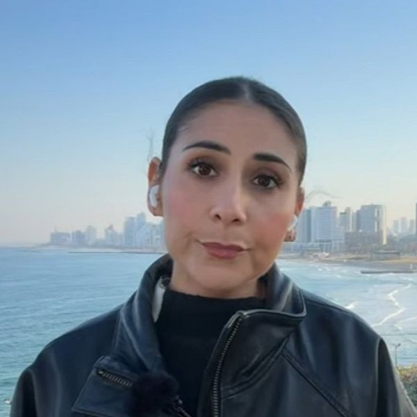 SVT:s korrespondent Gilda Hamidi-Nia vid havet med stadssilhuett i bakgrunden
