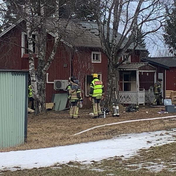 Brandmän undersöker rött hus med utrustning. Spår av snö på marken.