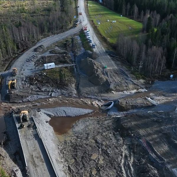 Vy över en byggarbetsplats med grönskande skog runt omkring. I bilden syns nya vägar som runnit sönder och maskiner som arbetar. En del av området är blöta och leriga, och det finns en sektion där vattnet rinner.