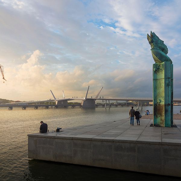 Göteborgs hamn vid solnedgång med skulptur och människor på kajen.