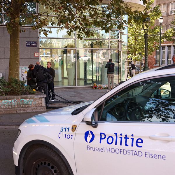 Belgisk polisbil och människor utanför bankkontoret där blommor lagts ner
