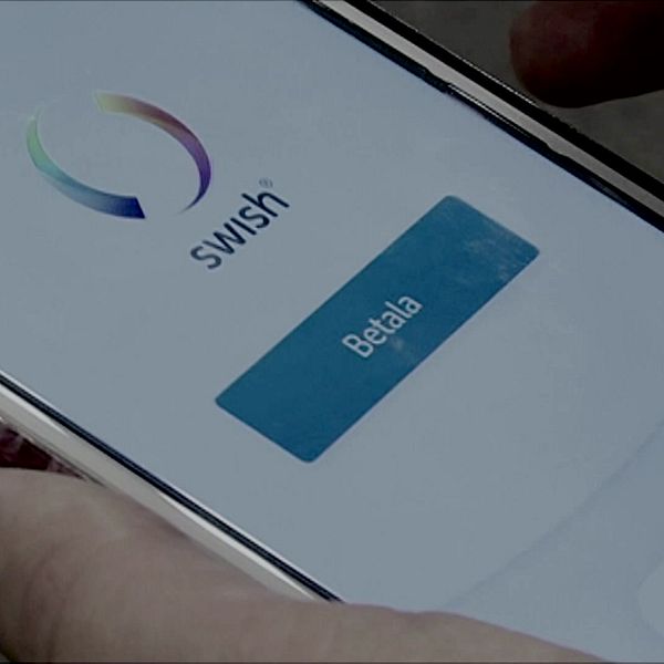 Mobilskärm visar Swish-appen med en knapp för att betala, medan en hand håller telefonen.