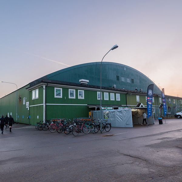 Grönt sportkomplex vid solnedgång. Cyklister och gående passerar på vägen.