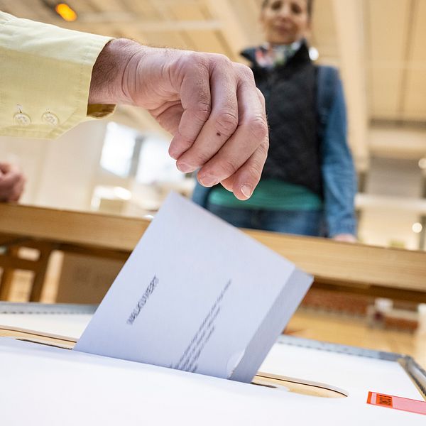 Person lägger valsedel i valurna i vallokal