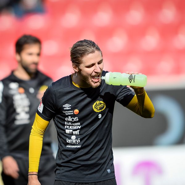 Pawel Cibicki  i svart och gult träningskläder håller en vattenflaska under en match på en stadion, med publik i bakgrunden.