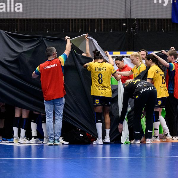 Handbollsspelare omringade av en svart duk på en inomhusplan.