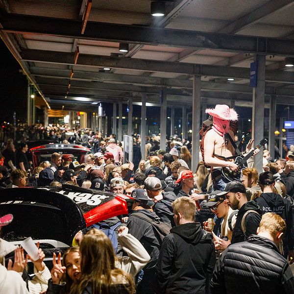 Folkmassa vid A6-parkeringen i Jönköping, en kille spelar gitarr iklädd ansiktsmask.