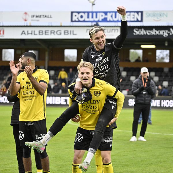 Fotbollsspelare i gula tröjor firar tillsammans på planen efter matchen.