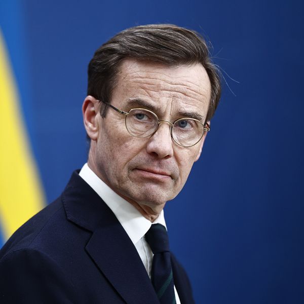 Statsminister Ulf Kristersson i kostym med svensk flagga i bakgrunden.