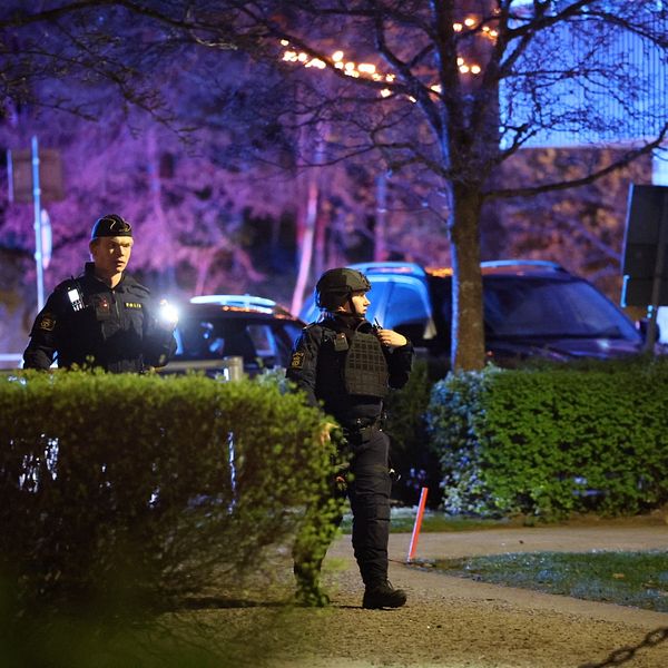 Två poliser arbetar avspärrat område utomhus med blåljus i bakgrunden på kvällen.