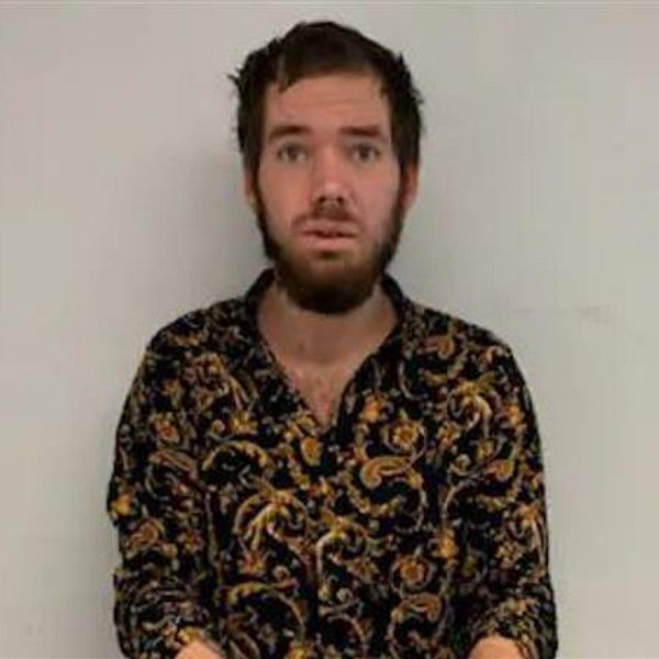 Person med mörkt, mönstrat skjorta står mot en vit vägg.