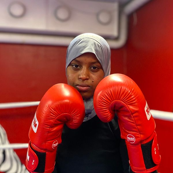 Tjej med hijab och boxningshandskar som står i en boxningsring och håller händerna i en fightposition.