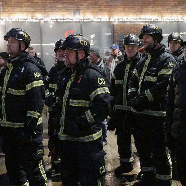 Brandmän i rad under manifestationen med publik i bakgrunden.