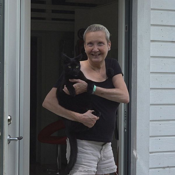 Kvinna håller sin katt i famnen och står i en dörröppning.