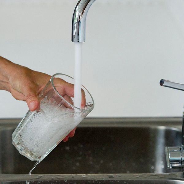 En person fyller ett vattenglas i köket.