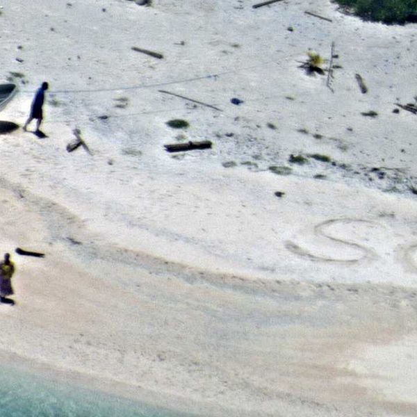 De två männen på stranden, med SOS skrivet i sanden.