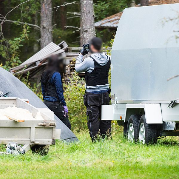 två poliser på en gård, släpvagnar och en traktor syns