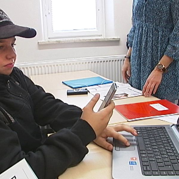 pojke med mobil och laptop i skolbänken