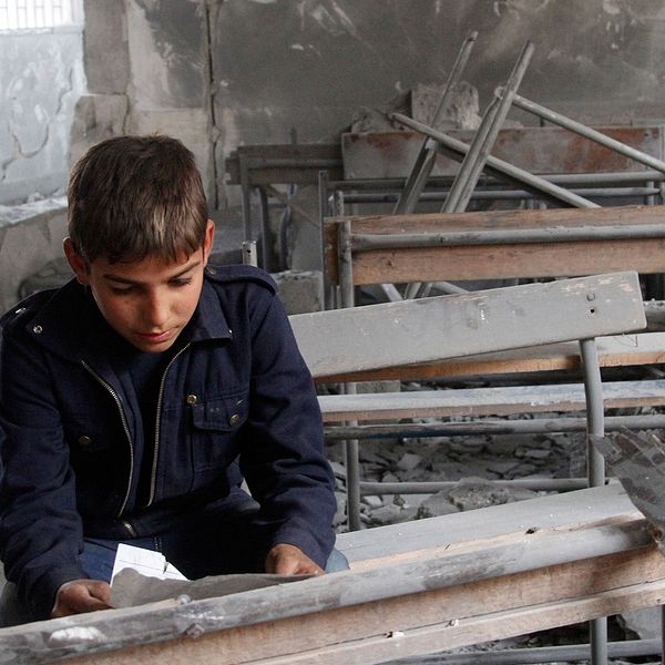 En syrisk pojke i sin sönderbombade skola i Syrien.