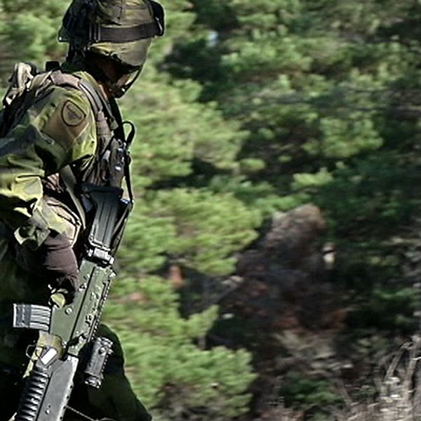 Soldat i uniform och vapen går i skog.